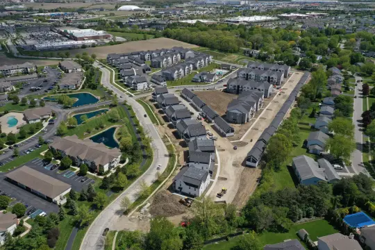 Aerial photograph of a townhome community partway through construction, with finished rows of homes, graded lots and earth-moving equipment beside an established neighbourhood.