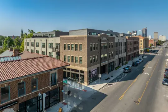 Elevated photograph of a brick apartment building lettered OGDEN with shopfronts along its ground floor, the downtown Columbus skyline in the distance.