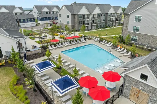 Aerial photograph of a swimming pool with red and navy umbrellas and rows of loungers, enclosed by gabled apartment buildings and townhomes.