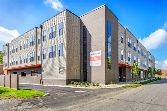 Street-corner view of a three-storey grey brick and shingle apartment building with orange canopies and a sign reading THE PEAKE.